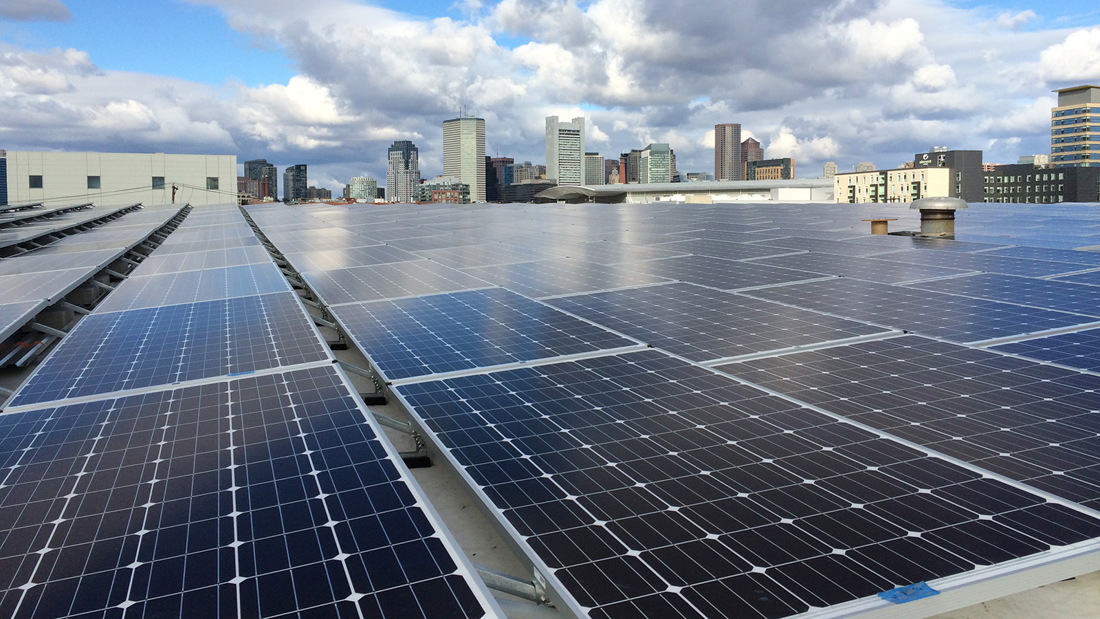 The Boston skyline is visible over the largest solar installation in Boston, located on a warehouse in the Seaport district