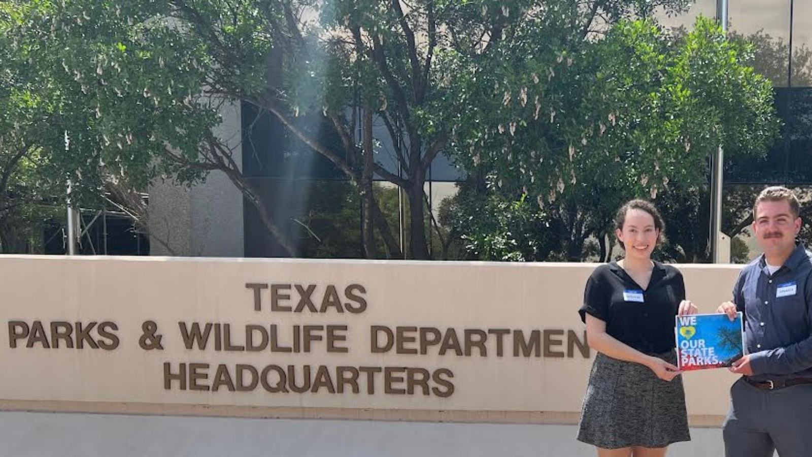 Environment Texas interns stand before Texas parks and wildlife department headquarters with sign saying 'we love our state parks'