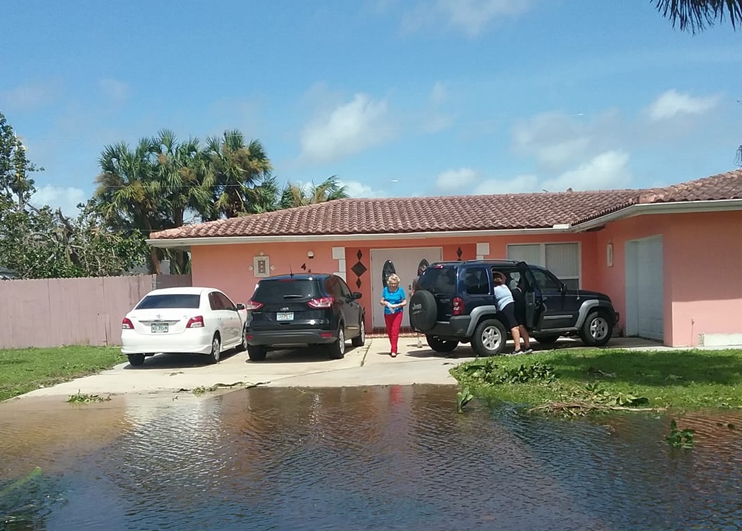 A flooded driveway in front of a house with people and parked cars