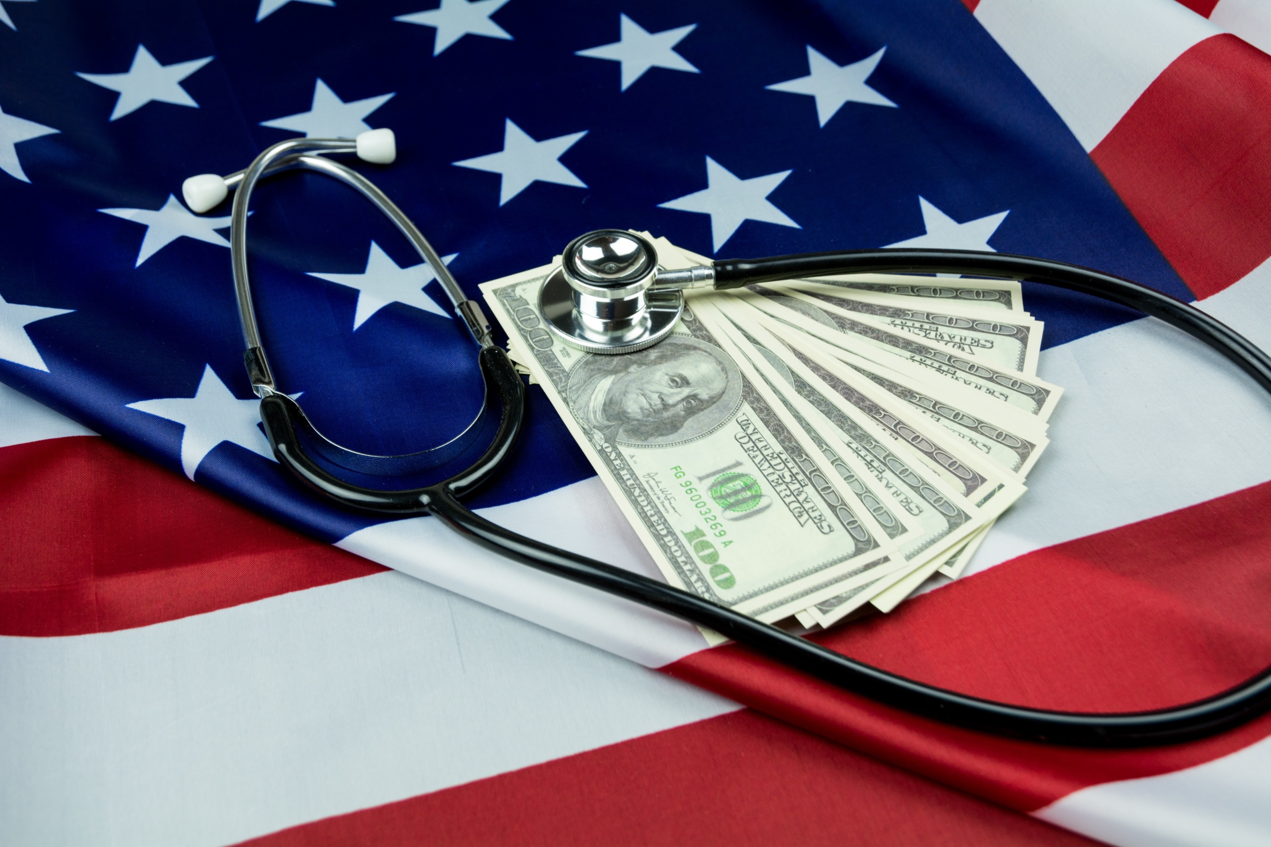 American flag under a stethoscope and pile of $100s