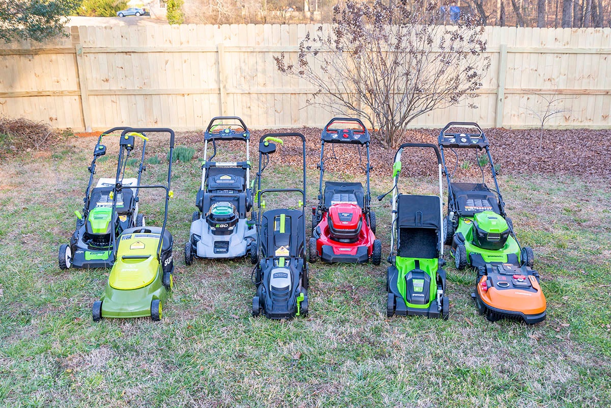 Eight different models of electric lawnmowers sitting on a green lawn.