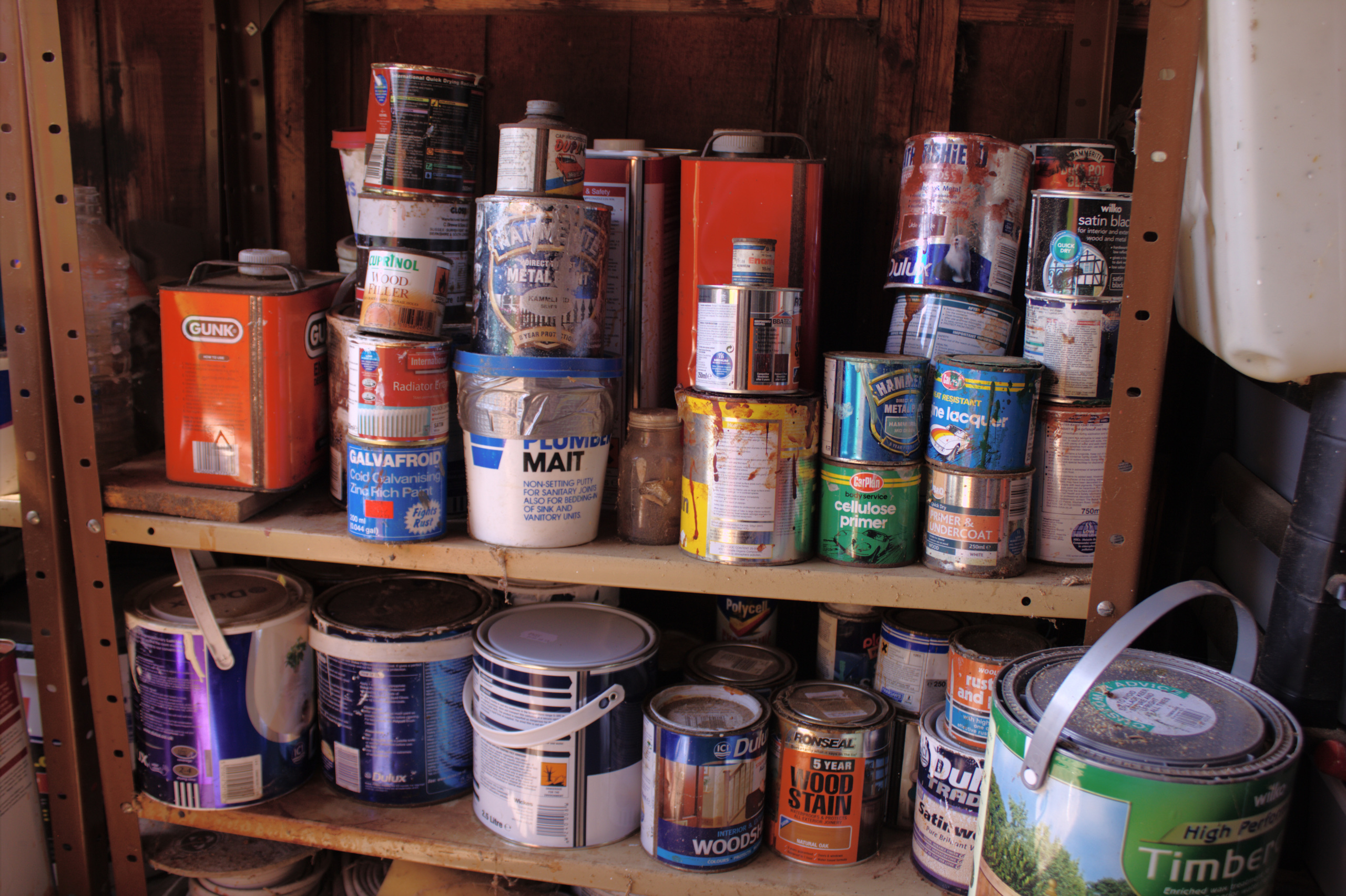 Cans of paint, wood stain and household chemicals on a wooden shelf.