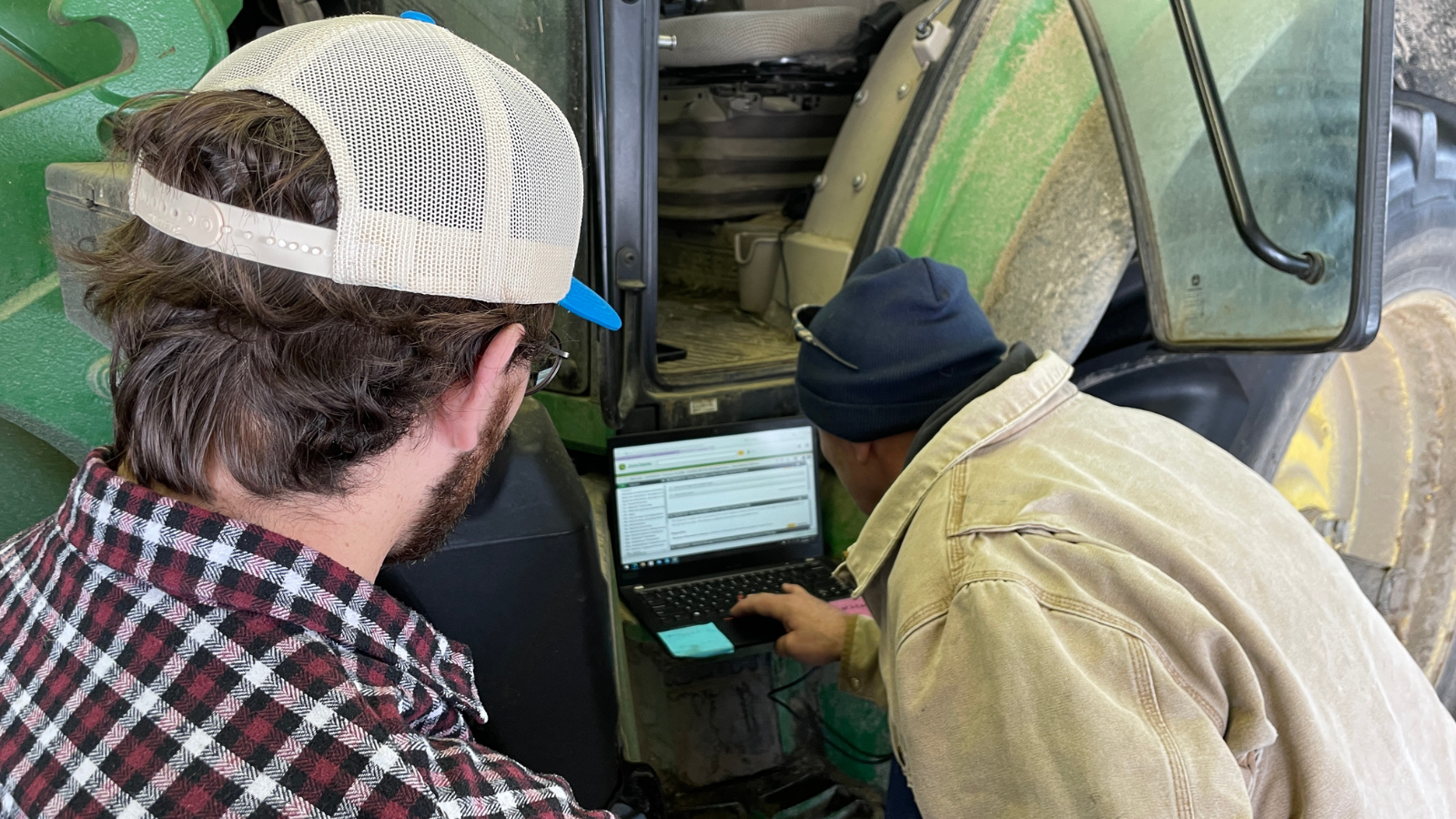 Right to Repair advocate Kevin O'Reilly and a mechanic look at Deere's software repair tools on a laptop connected to a green tractor