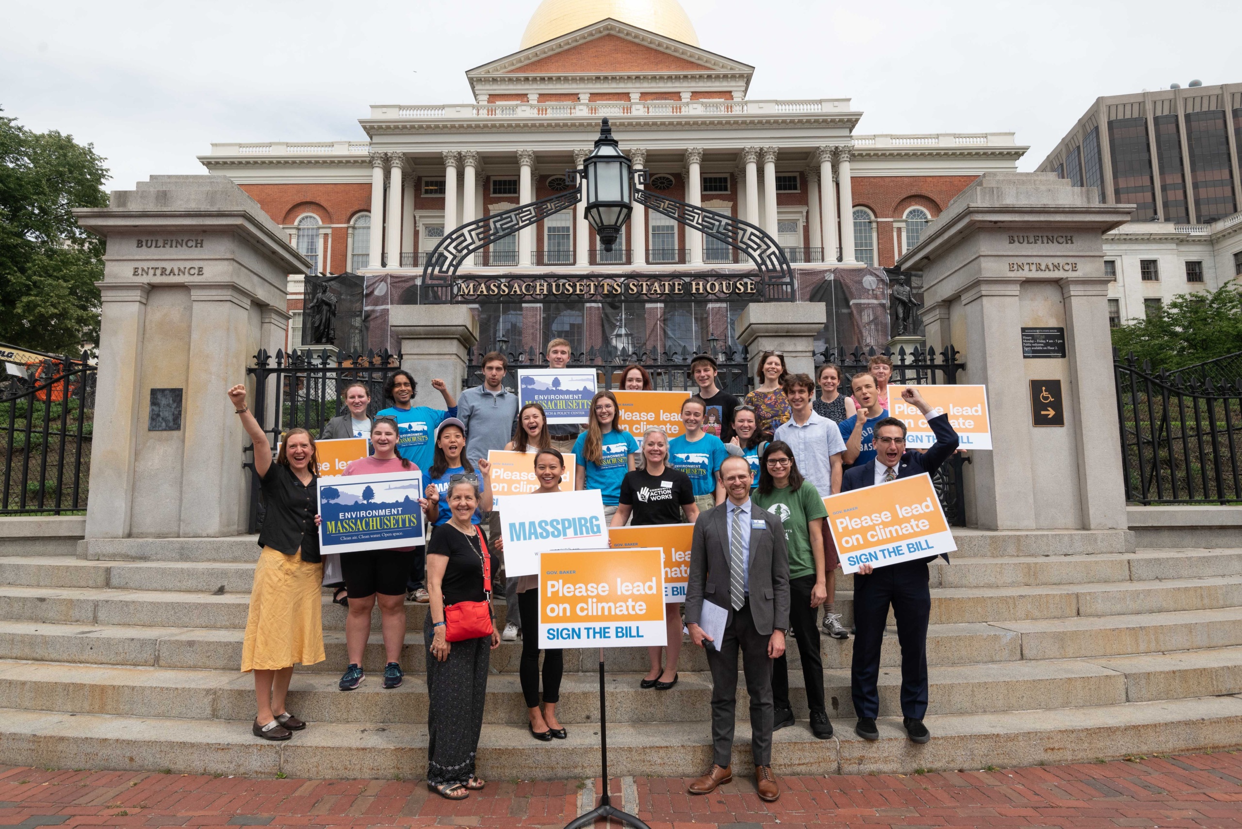 Activists rally on the steps of the Massachusetts State House, holding signs asking the governor to sign a climate bill.