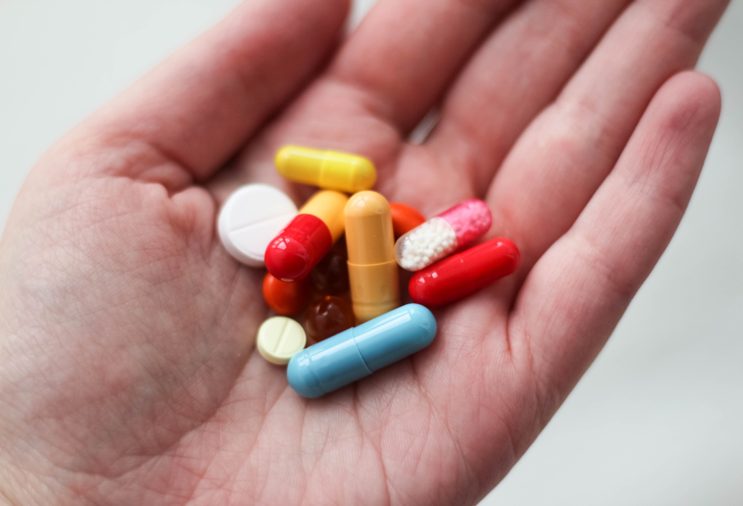 Hand holding multi-colored tablets and capsules