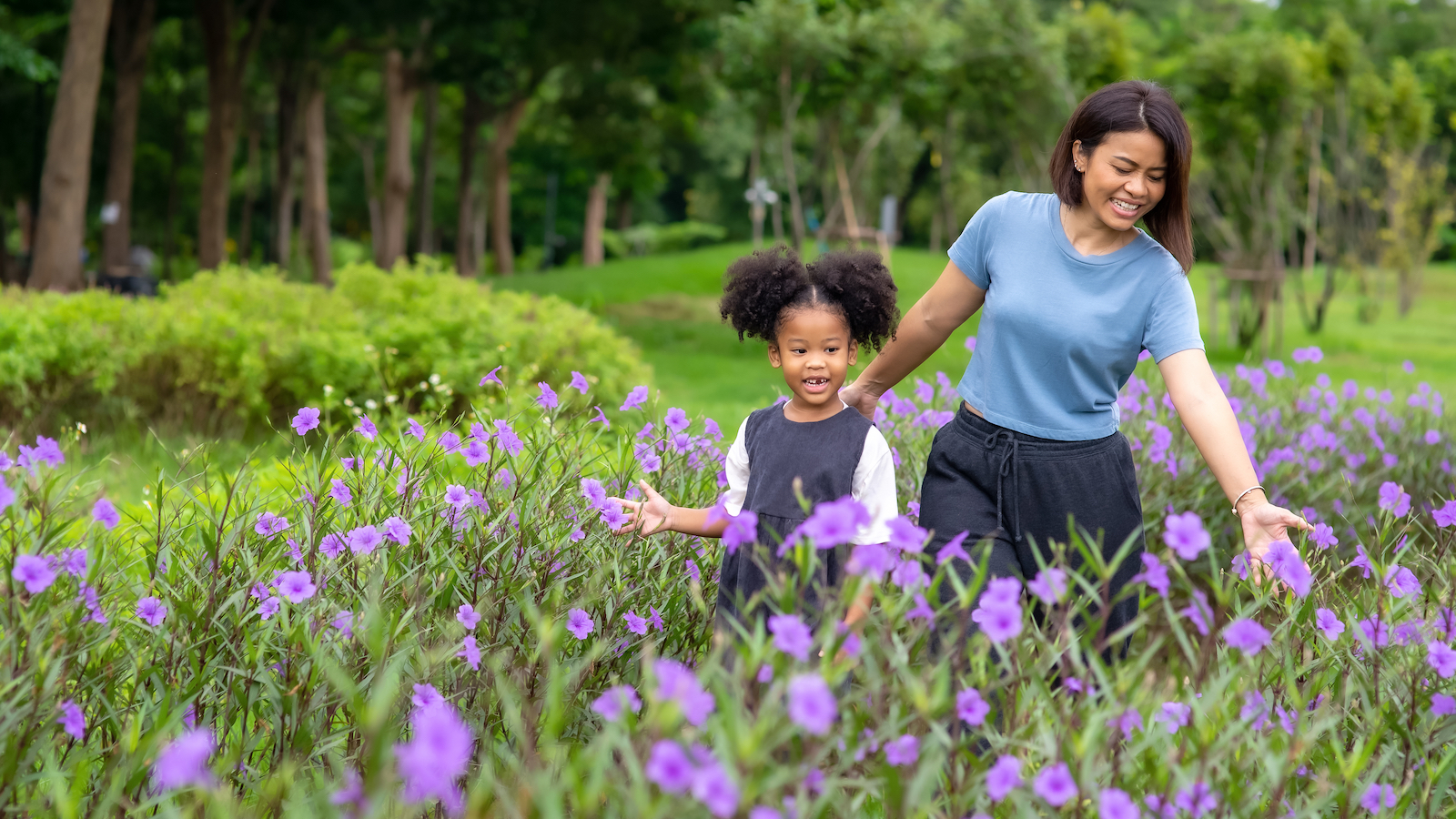 A woman and girl walk through a field of purple flowers.