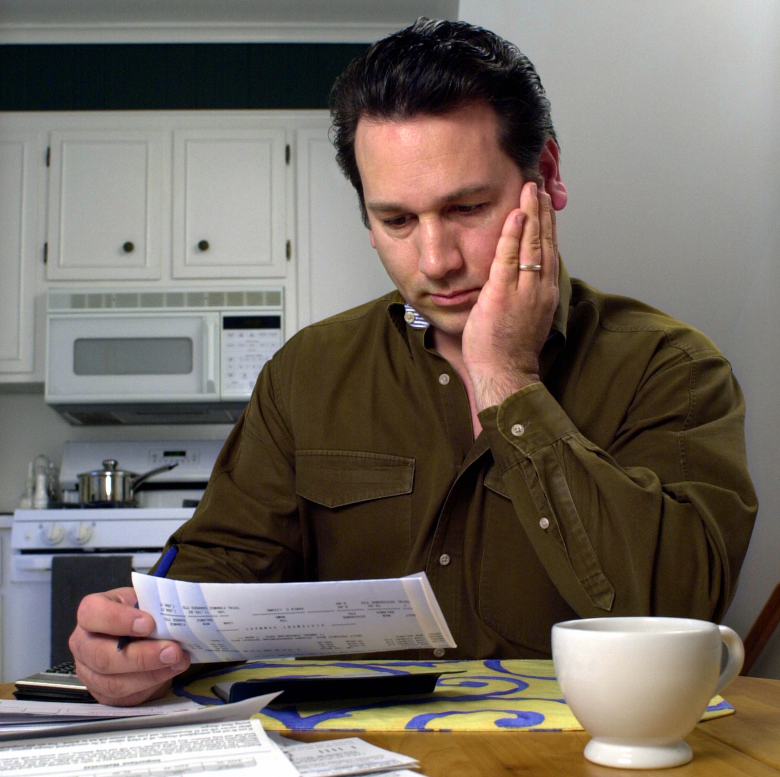 Caucasian man in brown shirt looking at paperwork in his kitchen