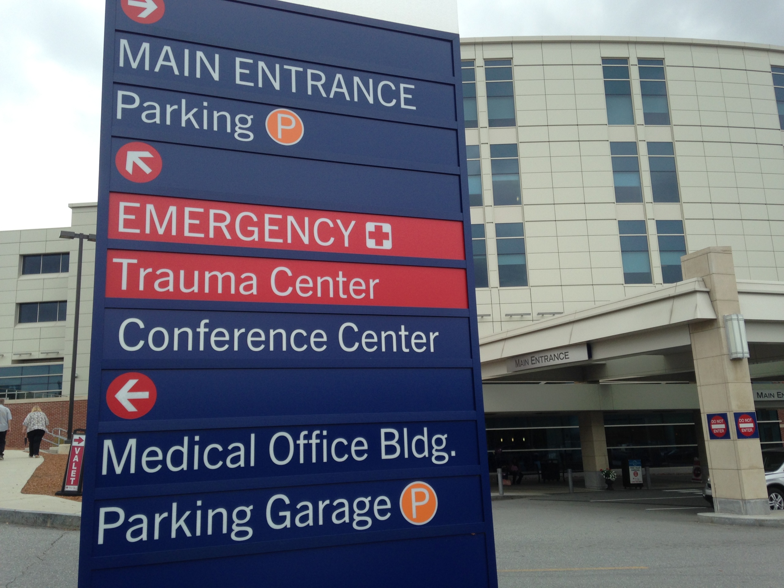 A sign in front of a hospital indicates where the main entrance, emergency room, and other destinations are located.