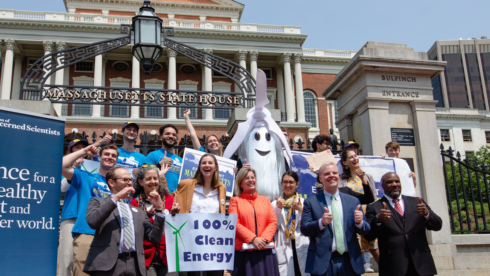 Legislators and climate advocates gather at the Massachusetts State House to celebrate a vision of 100% clean energy. A sign reads 