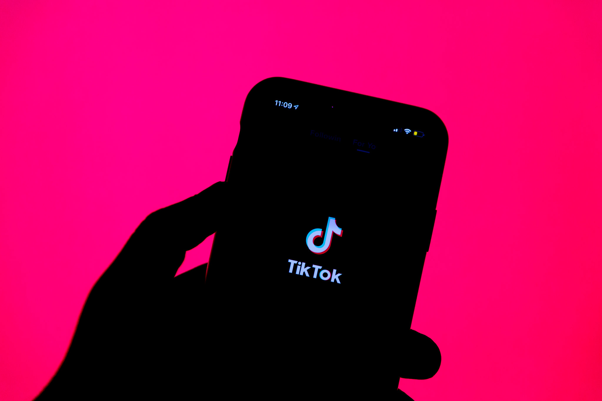 A silhouette of a person holding up a phone with the TikTok logo on a hot pink background