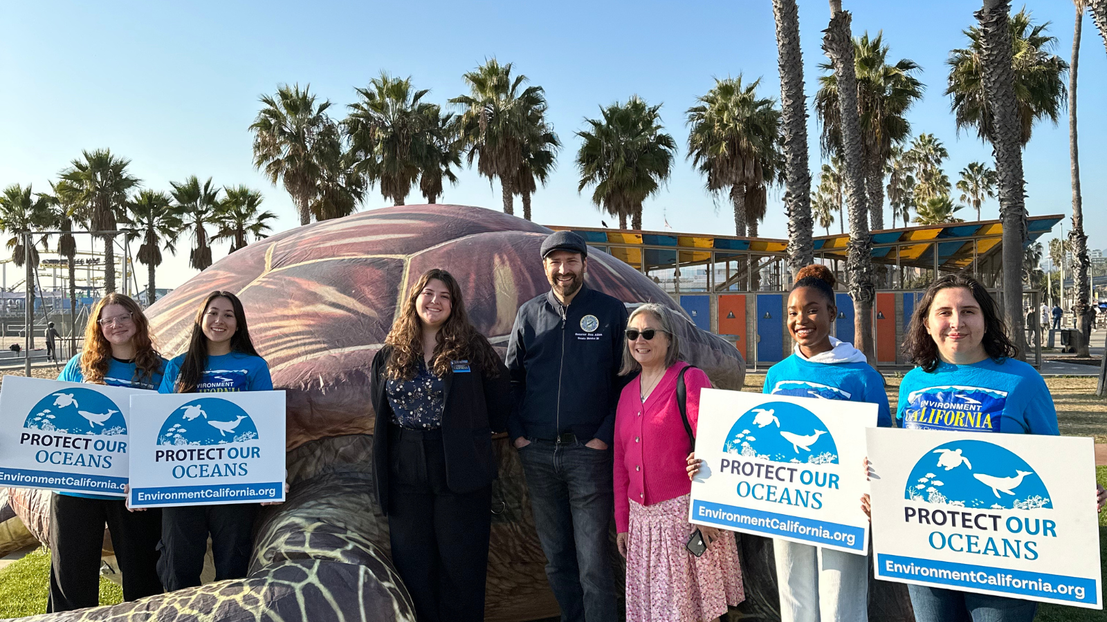 People in front of inflatable turtle with signs palm trees behind them