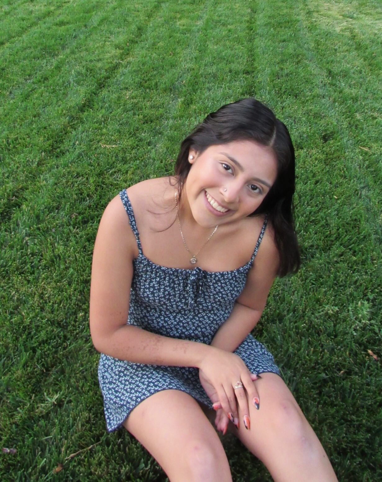 A photo of Emily, who's a student at the University of Oregon, sitting on the grass in a sundress.