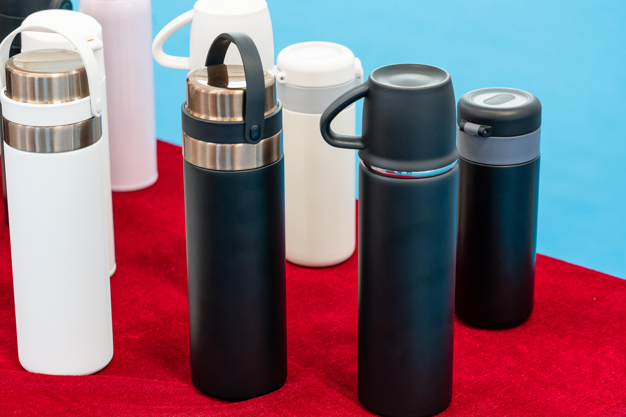 A variety of black and white reusable mugs and bottles on a red carpet