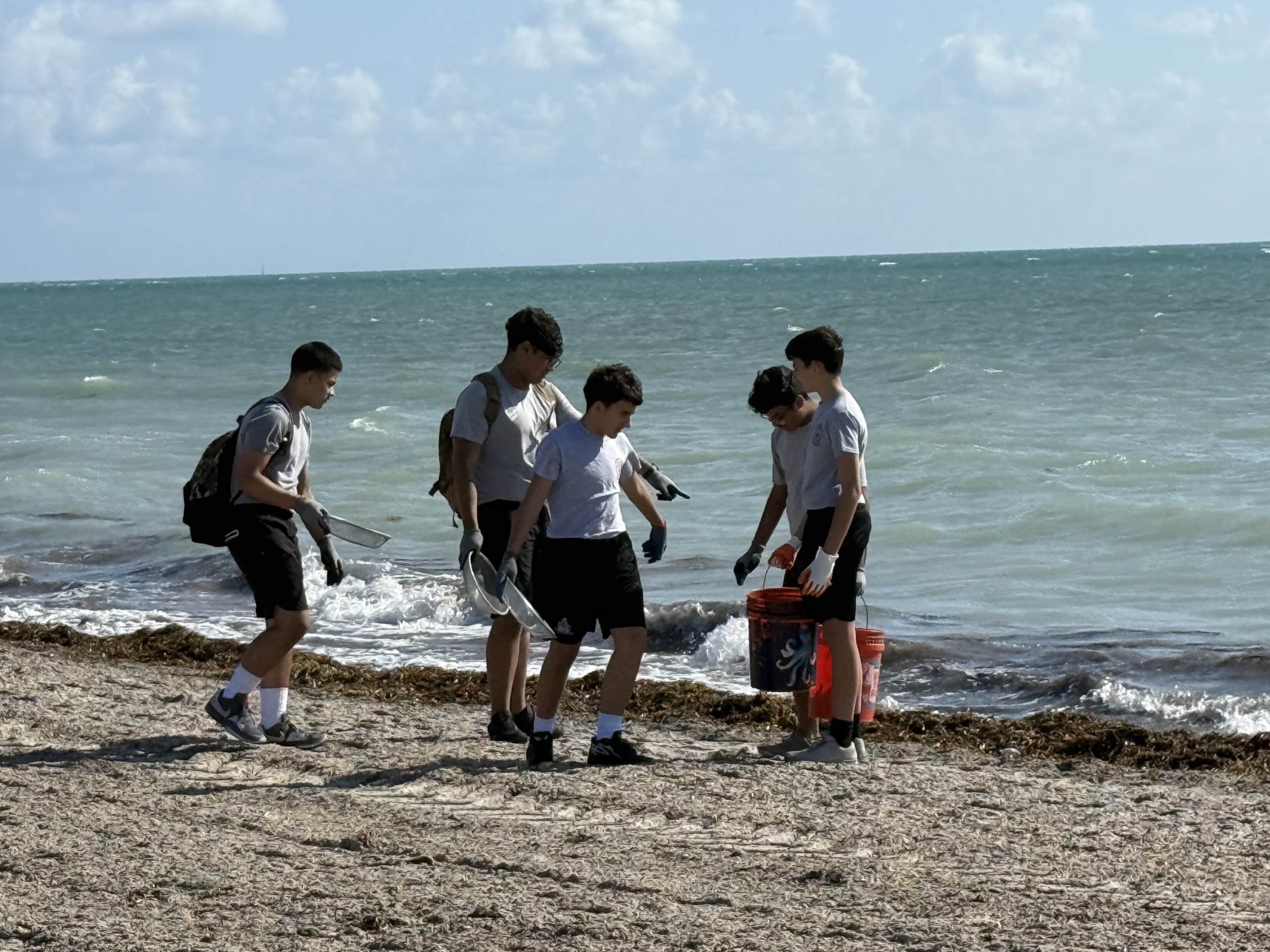 Students walk along beach with buckets for trash